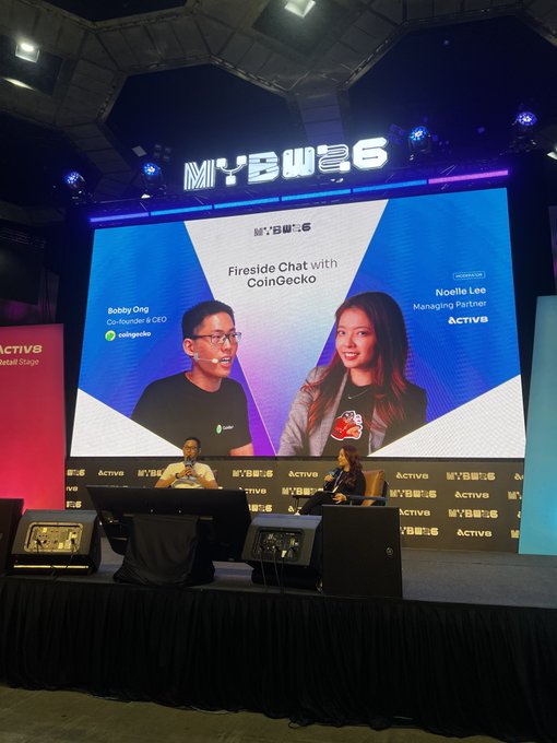 The image shows two speakers on stage at the Malaysia Blockchain Week (MYBW25) event during a "Fireside Chat with CoinGecko," featuring Bobby Ong (Co-founder & CEO of CoinGecko) and Noelle Lee (Managing Partner of Actva), directly matching the post about speaking at the conference.