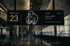 A photo of an airport information display showing "Gate 23" for a flight CX 562 to Tokyo (NRT) at 08:45, featuring a cartoon character mascot.
