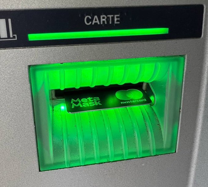 A MetaMask Mastercard branded black card inserted into an ATM card slot illuminated by a bright green glow, with 'CARTE' visible above.