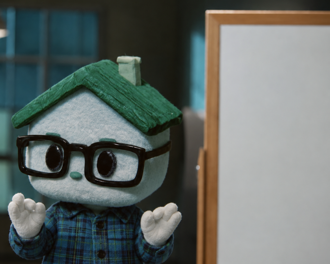 A plush mascot with a green roof-shaped hat, glasses, and a plaid shirt stands next to a blank whiteboard, hands raised in a shrugging gesture. The mascot's appearance suggests an investor or expert character, though the whiteboard is empty, reinforcing the post's joke about a fly being given $50 to trade on "pons" — implying no real strategy or content behind the plan.