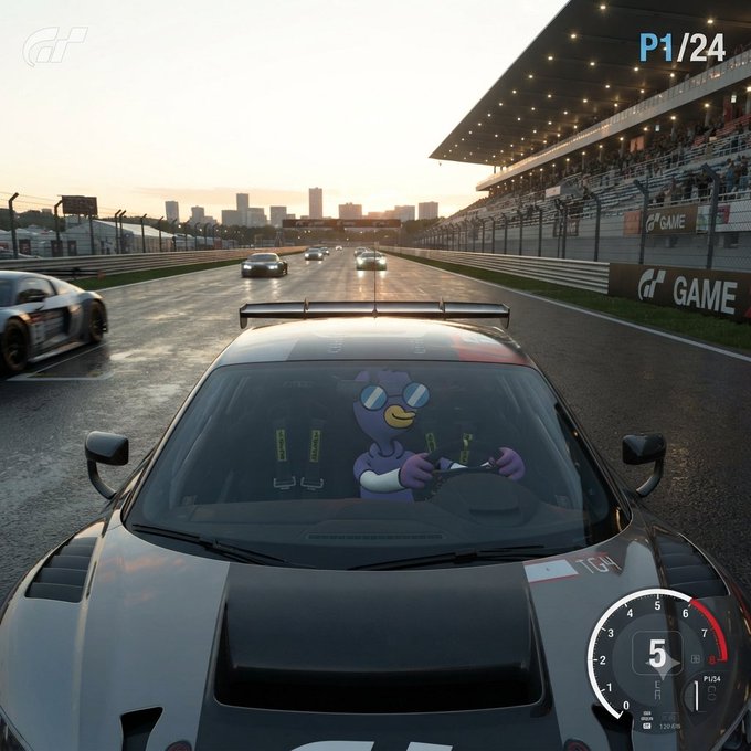 A screenshot from the racing video game Gran Turismo showing a first-person view from behind a car on a track, with a purple cartoon character visible on the windshield and 'P1/24' displayed in the top right corner.