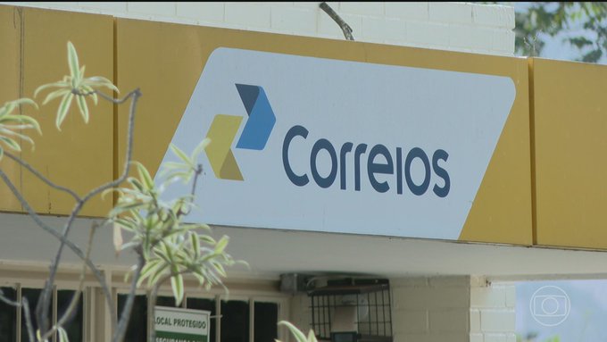 A Correios (Brazilian postal service) storefront sign is mounted on a yellow building facade, with branches of a plant partially obscuring the view. The post expressing extreme frustration likely relates to a negative experience with the postal service, such as a delayed or lost package, given Correios' reputation for unreliable delivery times in Brazil.