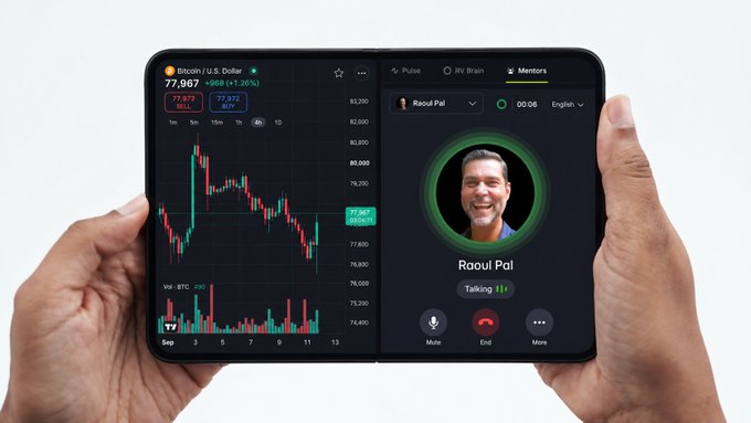 A pair of hands holds a foldable smartphone displaying a Bitcoin/USD trading chart priced at $77,967 alongside an active "Talk to Raoul Pal" AI mentor video call. The split-screen setup humorously illustrates the caption's premise, combining a bearish crypto crash chart with on-demand emotional support from the well-known macro investor.