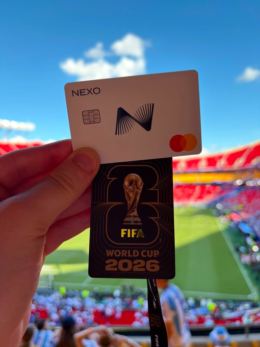 A hand holds up a NEXO Mastercard branded with the FIFA World Cup 2026 logo in front of a stadium's crowded stands, tying the card's tournament sponsorship to an exciting matchday experience shared with others.