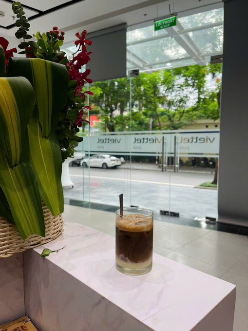 A glass of iced coffee with a straw sits on a marble countertop beside a lush green plant in a woven basket, while behind it, glass doors display the "Netter" logo—fitting fuel for the Wednesday grind referenced in the post.