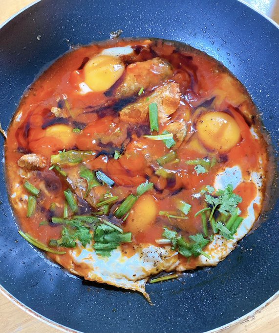 A pan containing a dish of poached eggs in a spicy red sauce, garnished with fresh cilantro and green onions.