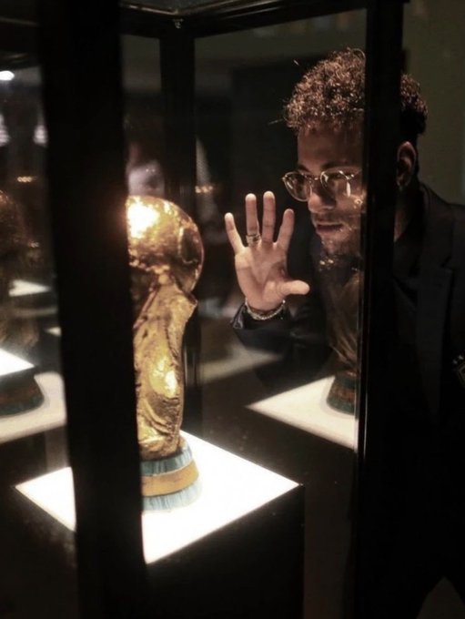 A photograph of a man wearing glasses looking through a glass display case at a golden, alien-like bust artifact illuminated from below.