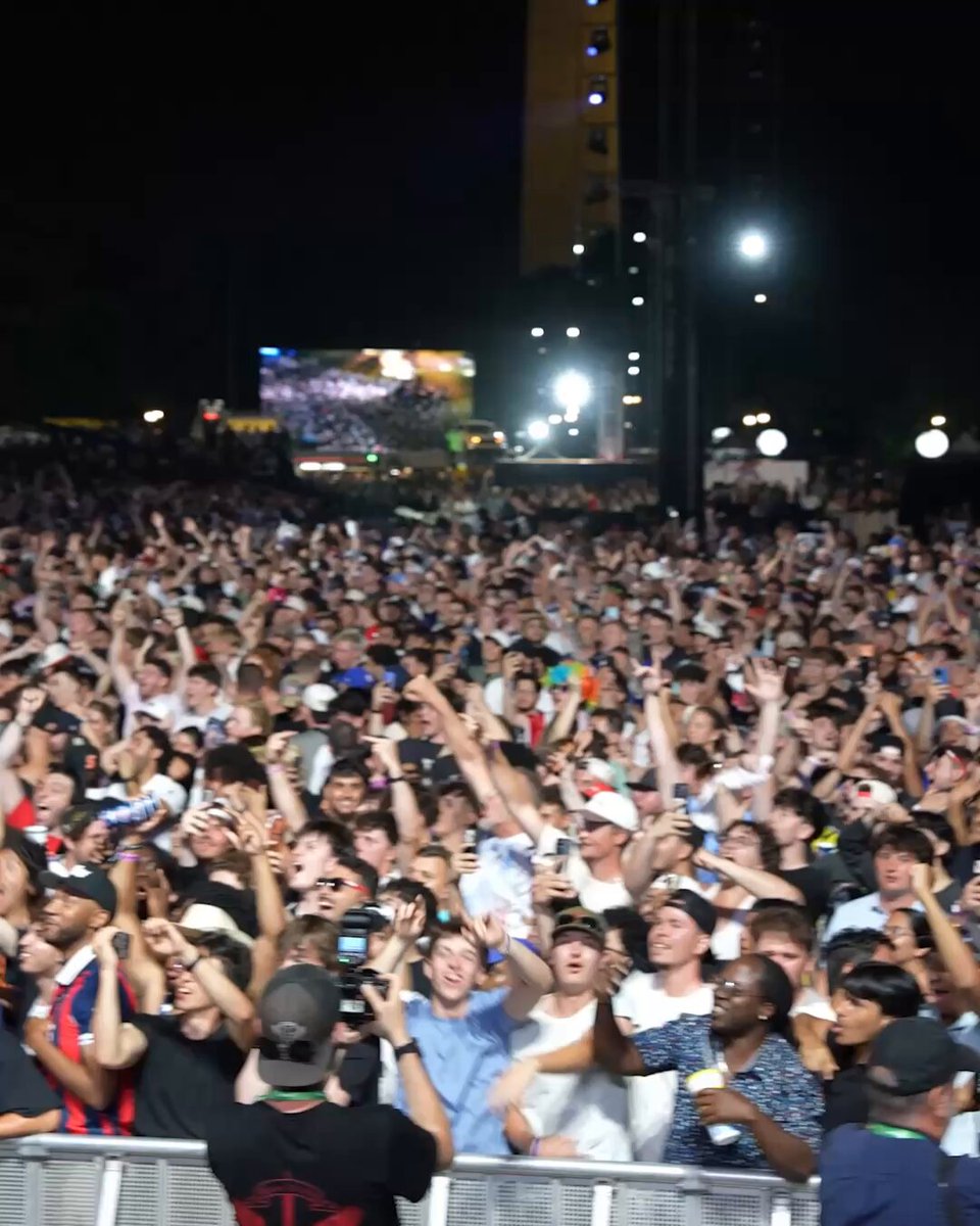 The image shows a large crowd of people gathered together, with many fans raising their arms up in excitement or celebration. The crowd appears to be at a concert or event, as they are all facing towards a screen that displays an image of UFC fighter # UFC White House. The atmosphere seems lively and energetic, with the fans enjoying themselves and showing their support for the fighters on the screen.