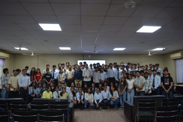 A group photo of a large class of students posing together in an auditorium or lecture hall with rows of empty seats visible.