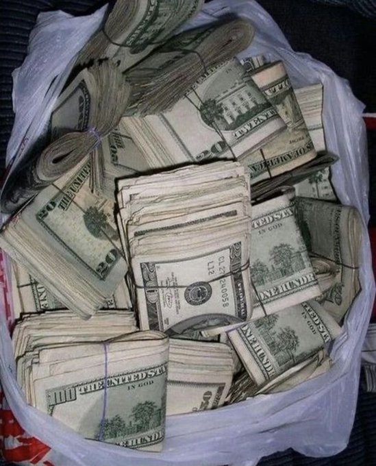 A plastic bag overflowing with rubber-banded stacks of US $20 and $100 bills—including visible "THE UNITED STATES OF AMERICA" and "PA 000584635 F2" markings—piles up in a bag, visually exaggerating the post's tongue-in-cheek birthday wish about striking it rich.
