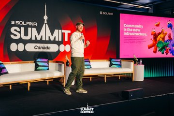 A speaker presents on stage at the Solana Summit Canada, with a large screen behind displaying "SOLANA SUMMIT Canada" alongside the tagline "Community is the new Infrastructure," and another screen reading "Consensus is the new infrastructure." The image captures the keynote moment referenced in the post, where Cabanimation addressed the audience on stage.