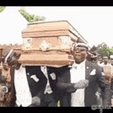 The image shows a group of people walking down a street, with one person wearing a suit and tie carrying an open wooden casket or coffin. The crowd appears to be gathered around this individual, possibly attending a funeral or memorial service. The scene suggests that there might have been a significant event in the past, as indicated by the presence of the casket.