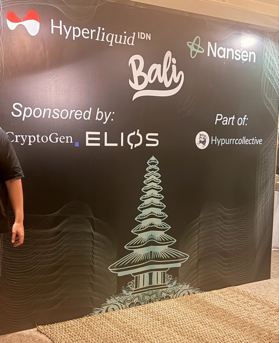 A person stands beside a promotional backdrop featuring a Balinese temple illustration with logos for Hyperliquid IDN, Nansen, CryptoGen, ELIOS, and Hypurrcollective, indicating it as sponsorship signage for a Hyperliquid-related event in Bali.