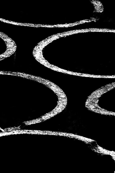 An abstract black and white image featuring several large, curved white chalk-like shapes against a dark black background.