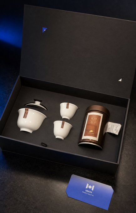 An elegant tea gift set presented in a black box, featuring a white porcelain gaiwan with cups and a dark canister labeled with Chinese characters, with an 'MIXN' branded card in front.