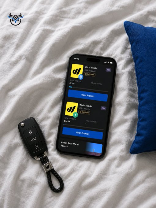 A smartphone resting on a bed displaying the World Mobile app interface with "Open Position" options, placed next to a Volkswagen car key fob and a blue pillow.