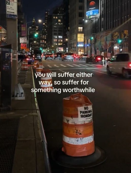 A nighttime city street scene features an orange and white "NO PARKING MONDAY" traffic barrel in the foreground, with city lights, cars, and buildings in the background, overlaid with the text "you will suffer either way, so suffer for something worthwhile."

The image pairs with the post's message about perseverance by symbolizing life's obstacles—much like the construction barrel blocking the path—reminding viewers that struggle is inevitable, so it should be directed toward goals that truly matter.