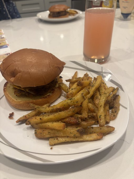 A meal featuring a cheeseburger with a generous portion of seasoned fries on a white plate, accompanied by a glass of pink-hued lemonade, with another burger visible in the background. The caption "Gn web3" suggests a casual goodnight post, with the hearty comfort meal serving as a dinner scene to wrap up the evening.