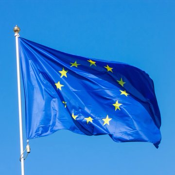 The European Union flag waves against a clear blue sky, symbolizing the EU's recent proposal to grant Canada "associate member" status—marking a historic expansion of the bloc's diplomatic ties.