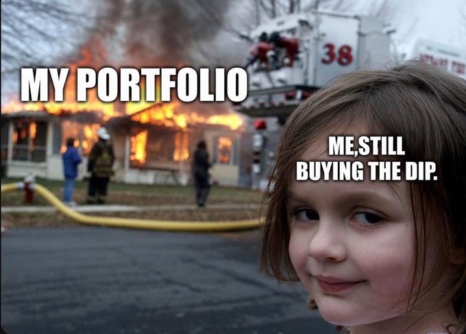 A young girl smirks calmly while a house labeled "MY PORTFOLIO" burns in the background behind firefighters, with the text "ME, STILL BUYING THE DIP" overlaid on her face—capturing the meme's joke of remaining optimistic about investing even as one's holdings go up in flames.