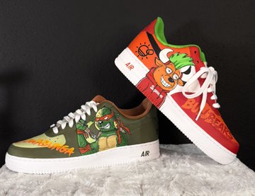 A pair of custom-painted low-top sneakers featuring Teenage Mutant Ninja Turtles artwork, with one shoe in olive green/white and the other in red/white, branded with 'AR'.