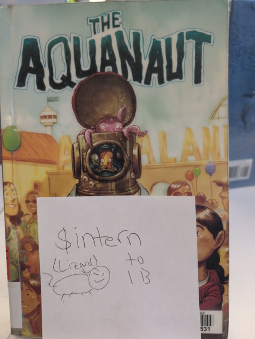A comic book titled "THE AQUANAUT" with a handwritten note attached to it that says "$intern (lizard) to 1B" with a small drawing of a smiling lizard.