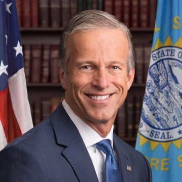 An official portrait shows Senator John Thune, identified by the U.S. and South Dakota state flags with the "STATE OF SOUTH DAKOTA" seal visible behind him, smiling in a navy suit and blue tie. The image accompanies news that Senate Majority Leader Thune has filed for cloture on the CLARITY Act, setting up a Senate floor vote in September.