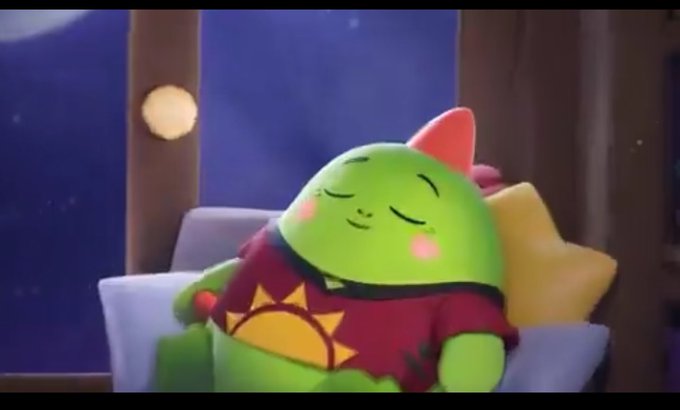 A green cartoon character with closed eyes and blushing cheeks, wearing a maroon sweater with a sun design, sitting against a starry night background with a crescent moon.