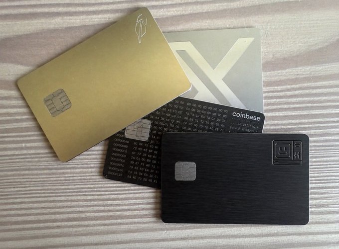 A collection of cryptocurrency cards including a gold card and black cards arranged on a wooden surface, with one displaying 'coinbase' and binary code patterns.