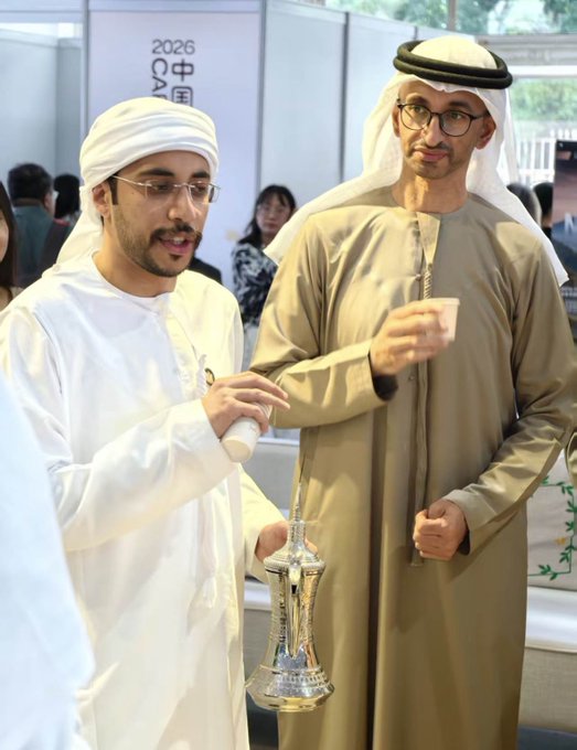Two men in traditional Emirati attire pose near a silver trophy, with a sign reading '2026 EXPO 中国' partially visible in the background.