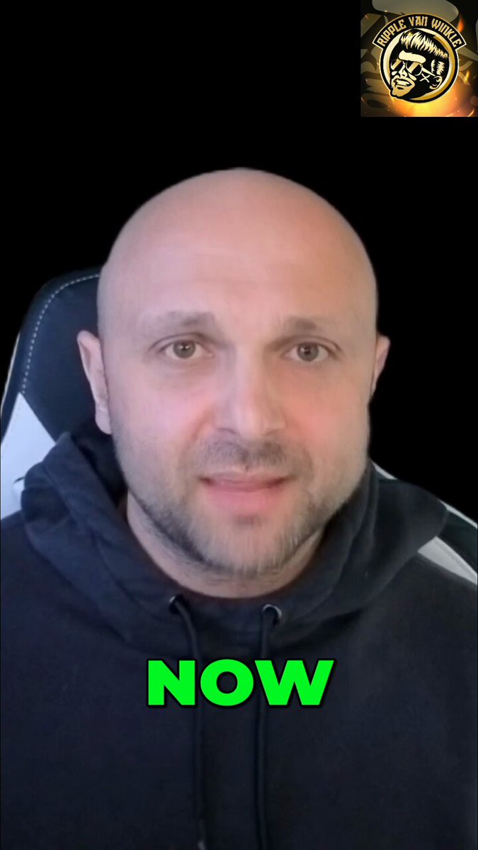 The image shows a bald man wearing a black hoodie, sitting in front of a computer screen with a green text box that reads "Now" and "XRP". The background appears to be a dark color, possibly a wall or a window frame. The image also contains some text about XRP and how it can help solve the problem of frozen bank accounts by providing instant payments.