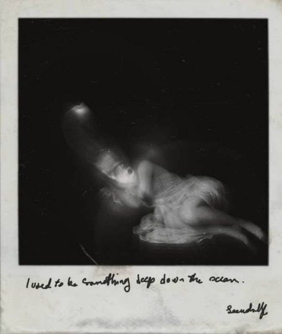 A dark, blurry Polaroid-style photo with handwritten text reading "I used to be something deep down the ocean" signed "Scribbly".