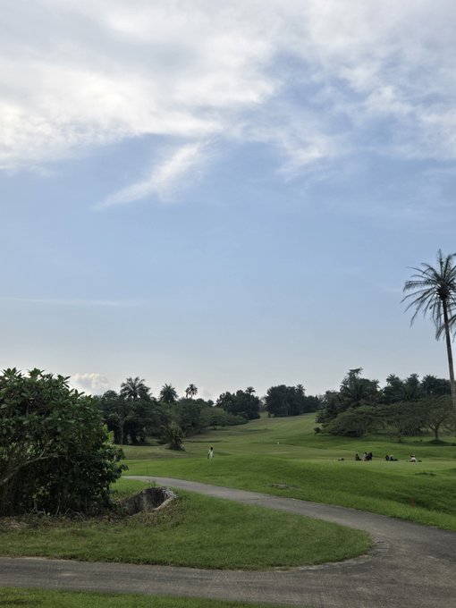 A golf course stretches under a cloudy sky with a few players visible in the distance, while a paved path curves through the foreground. The serene green landscape humorously contrasts with the chaotic "schedule" of job hunting, trading Solana, and chasing 100x gains—suggesting the calm vibes are far from this poster's reality.