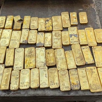 A collection of gold bars stamped with serial numbers and assay marks lies scattered across a surface. The image humorously illustrates the idea of "finding" wealth, contrasting the traditional gold bars with the post's joke about stumbling upon a 10 BTC wallet and immediately cashing out to Coinbase for taxes.