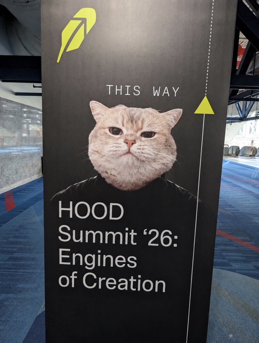 A directional sign at the "HOOD Summit '26: Engines of Creation" features a cat in a black hoodie with the text "THIS WAY" and a yellow arrow, placed in a carpeted hallway. The image appears unrelated to the accompanying text discussing $VRAX token analysis and a specific CA (contract address) on Twitter.