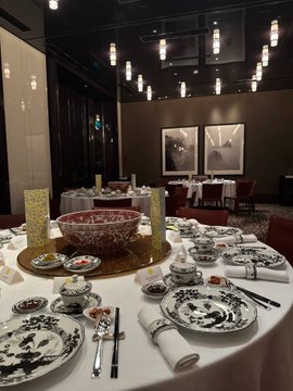 A dimly lit, upscale Chinese restaurant interior with round tables set with elegant blue-and-white porcelain dishes, chopsticks, and decorative bowls.