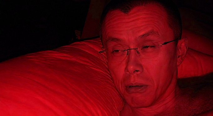 The image shows an older Asian man wearing glasses lying on a pillow, bathed entirely in red lighting. The post references "CZ," referring to Changpeng Zhao, the founder of Binance cryptocurrency exchange, though the person pictured does not appear to match his known appearance.