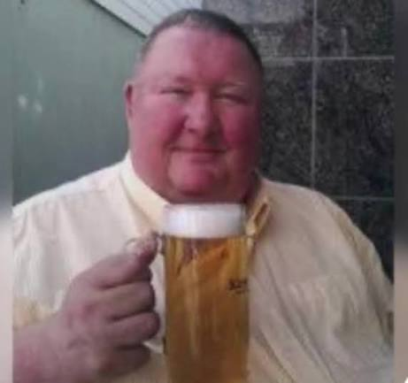 A cheerful, ruddy-faced man smiles while raising a frothy pint of beer, fitting the post's self-deprecating humor about a Nokia (NOK) holder's mundane British day—complete with a lukewarm full English and a drive in his old Vauxhall Astra.