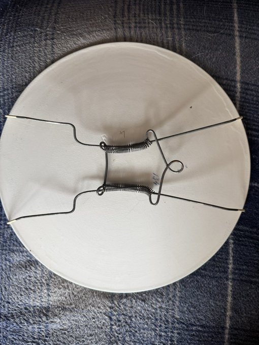A simple, functional spring-clip hat accessory made of wire rests on a white plate placed over a gray plaid fabric.