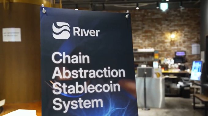 The image shows a poster or sign hanging on a wall with the words "RIVER" written on it. The poster also contains information about a stablecoin system that has been recently updated, which might be of interest to cryptocurrency enthusiasts.