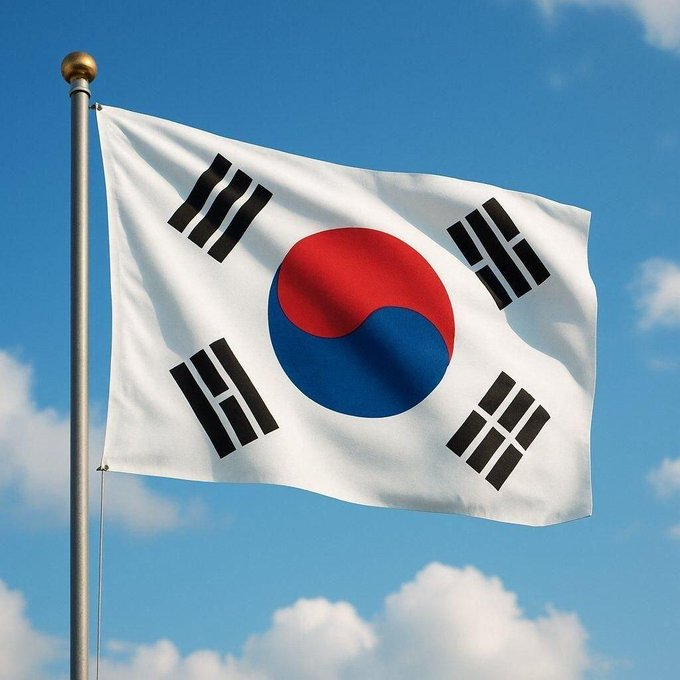 The South Korean national flag, featuring the iconic red and blue taegeuk symbol and four black trigrams on a white background, waves against a partly cloudy blue sky. The image visually anchors the news about South Korea's crypto tax delay petition surpassing 50,000 signatures, symbolizing the country at the center of the ongoing legislative debate.