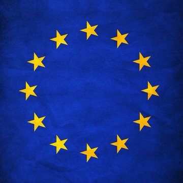 The European Union flag with twelve yellow stars arranged in a circle on a blue background, displayed on wrinkled fabric.