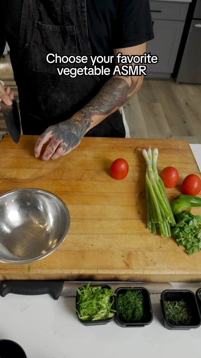 A top-down view of a person with tattooed arms preparing food on a wooden cutting board, featuring tomatoes, scallions, cilantro, a green chili, and a metal mixing bowl, with text overlay reading "Choose your favorite vegetable ASMR".