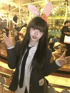 A young woman with long dark hair wearing a school uniform and pink bunny ear headband, posing with peace signs in what appears to be a cafe or restaurant.