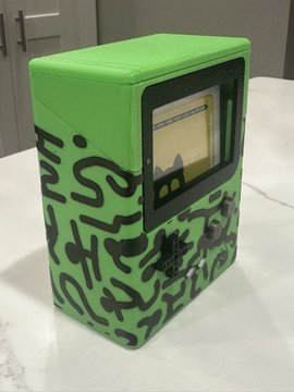 A small green box or safe decorated with black abstract line drawings, featuring a clear window on the front and a silver combination lock dial.