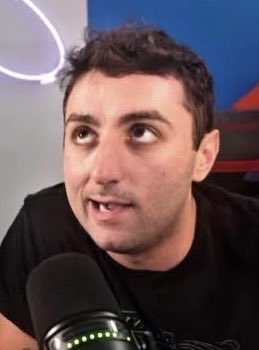 A man with dark hair and a black t-shirt speaks into a microphone during what appears to be a podcast, set against a blue background. The image accompanies a post noting that Rasmr has stated multi-wallet activities shouldn't be considered bad because "all the wallets are public."