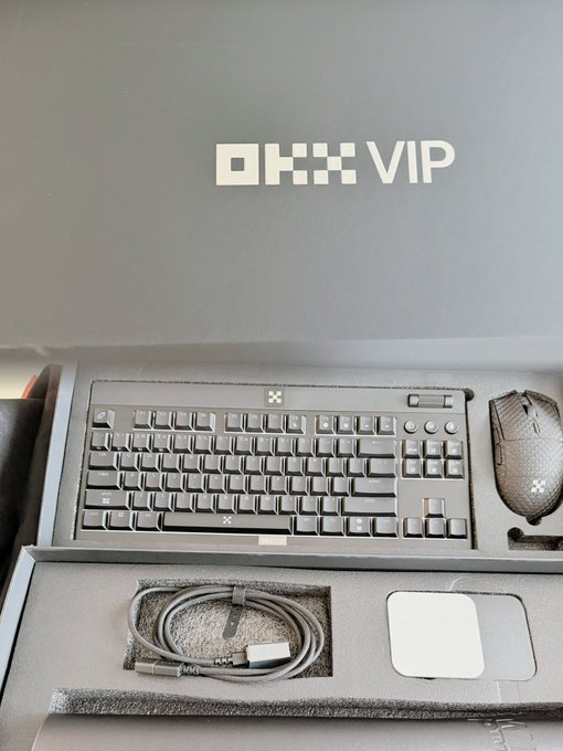 An unboxing of an OKX VIP promotional package containing a premium keyboard, gaming mouse, and cables neatly arranged in a branded box.