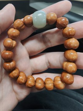 A hand holds a bracelet made of round wooden beads with a single white jade bead.