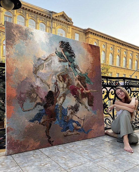 A young woman sitting barefoot on a balcony next to a large classical-style painting depicting dynamic, dancing figures in flowing fabrics, with an ornate yellow building in the background.