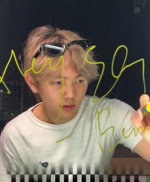 A young man with light brown hair wearing sunglasses on his head and a white t-shirt, with yellow handwritten text overlaid that appears to read 'Any Song' along with other markings.